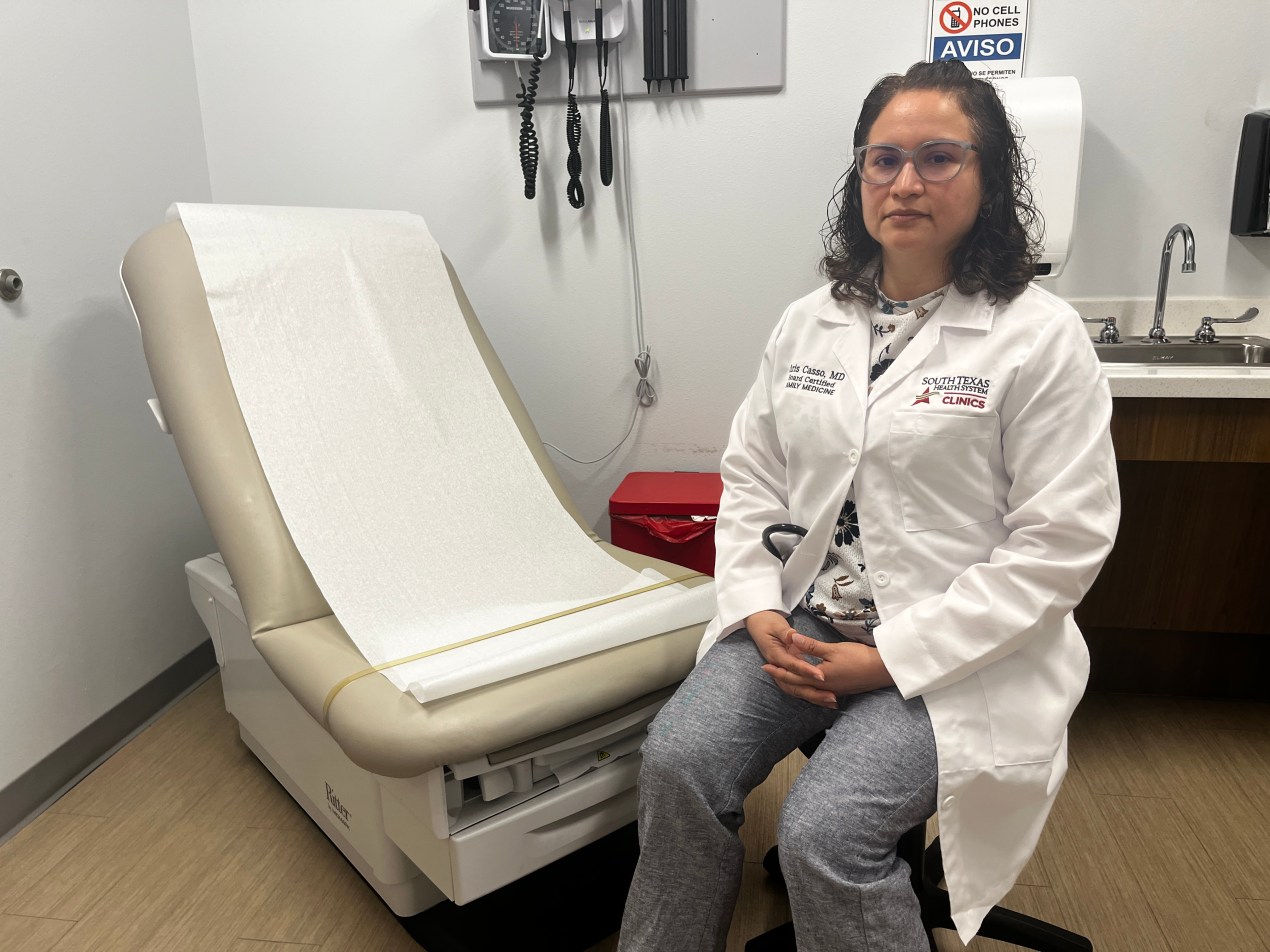 A photo of a doctor sitting by an exam chair in her office.