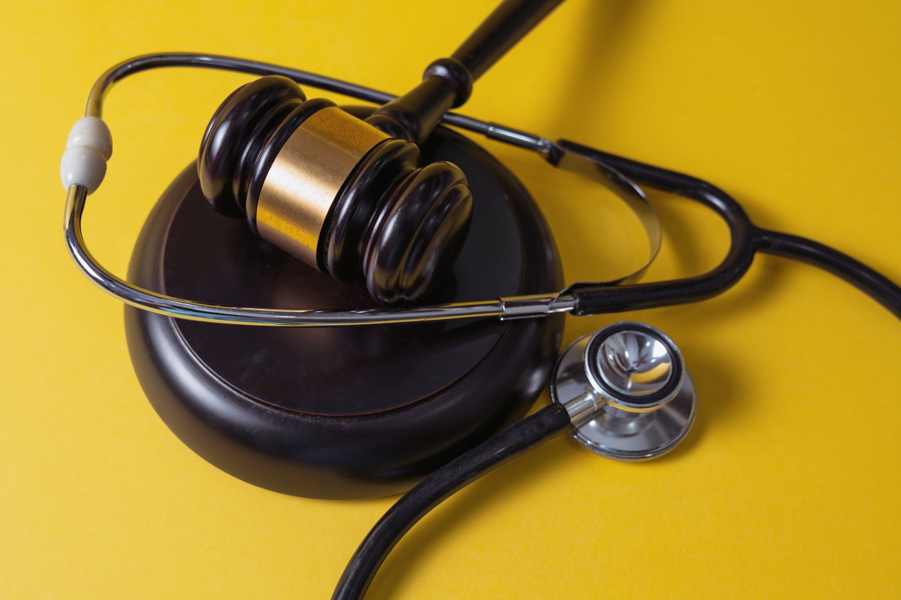 A gavel and stethoscope on a yellow background.